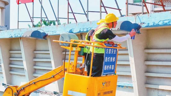 工作人员拆卸更换外墙的老化灯具。